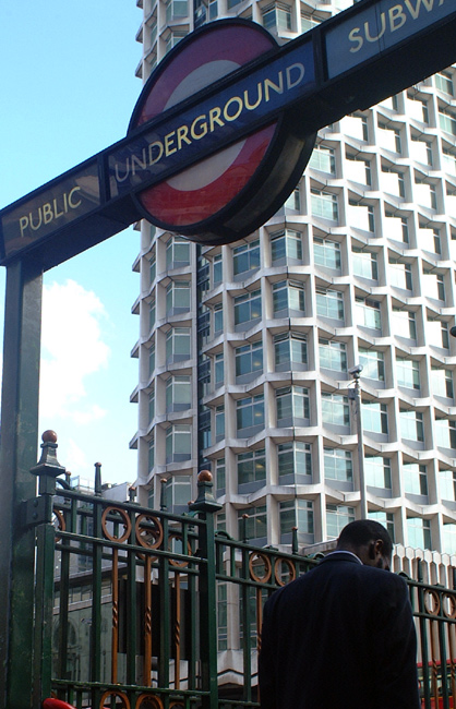A London resident enters a Tube (Subway) station against the backdrop of a smart looking apartment building.  London, U.K.