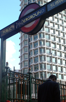 A London resident enters a Tube (Subway) station against the backdrop of a smart looking apartment building.  London, U.K.